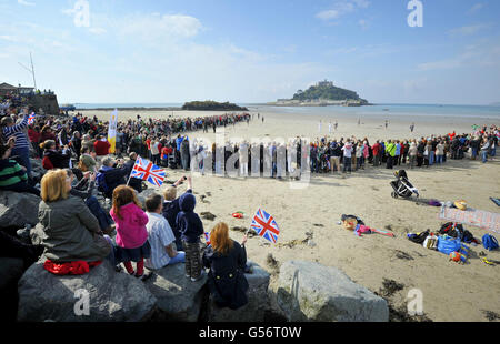 Les foules observent que Sarah Blight passe la flamme olympique à un porte-flambeau (nom non donné) sur la plage de Marazion, en Cornouailles, en regardant vers le mont St Michael's, pendant la branche du relais de la torche entre Newlyn et Marazion. Banque D'Images