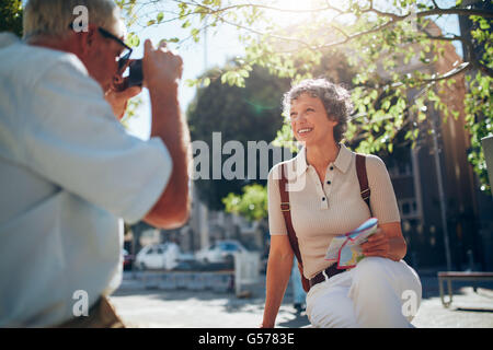Man locations de photographies de sa femme. Belle senior woman posing for camera assis dehors sur un banc je Banque D'Images