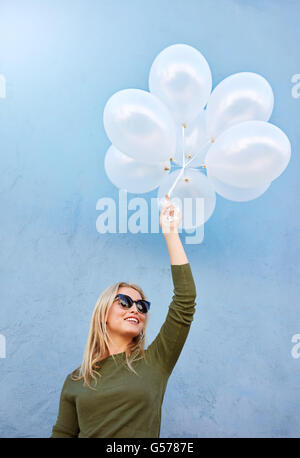 Coup de jeune joyeuse modèle féminin avec des ballons. Caucasian woman in sunglasses contre fond bleu. Banque D'Images