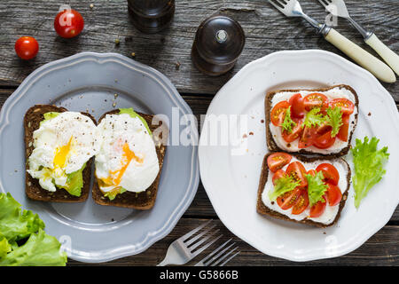 Divers toasts sain : oeuf poché, avocat, fromage frais, tomates, basilic et salade. Assiette de collations santé Banque D'Images