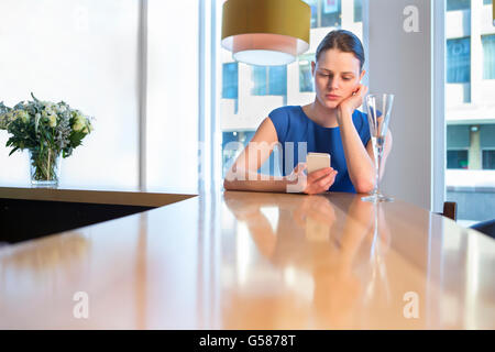 Jeune femme assise au bar avec un verre de champagne, à l'aide de son smartphone. Banque D'Images