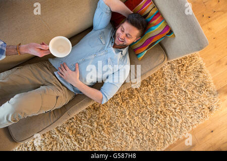 Homme détente sur la canapé. Son bras est dans le partenaires tourné avec une tasse de café vide dans sa main comme il l'enlève. Banque D'Images