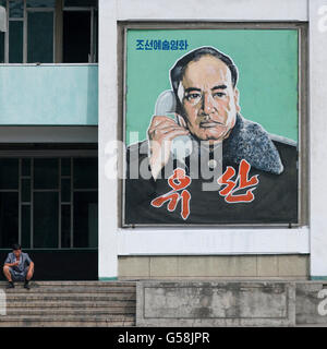 La Corée du Nord, Comté de Pyeongchang, Corée du Nord, Pyongyang man looking at mobile phone devant un film affiche représentant un Banque D'Images