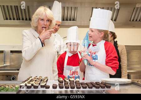 La duchesse de Cornwall se régale de son pouce alors qu'elle rencontre Cory Hogg (au centre) et Katie Elder, élèves de l'école primaire d'Eastington, Gloucestershire, dans les cuisines de Buckingham Palace, dans le centre de Londres. Banque D'Images