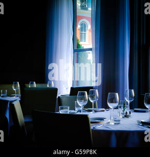 Une faible lumière de l'intérieur de tables avec nappes élégantes dans une salle à manger avec de la vaisselle et des verres à vin avec windows Banque D'Images