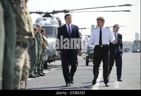 Le Premier ministre David Cameron est escorté par le capitaine Andrew Betton lors d'une visite au HMS Ocean sur la Tamise pour rendre hommage à l'implication du navire et de son équipage dans la sécurité olympique. Banque D'Images