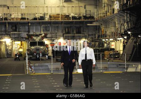 Le Premier ministre David Cameron est escorté par le capitaine Andrew Betton dans le hangar du HMS Ocean sur la Tamise pour rendre hommage à l'implication du navire et de son équipage dans la sécurité olympique. Banque D'Images