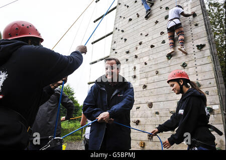 Le Premier ministre David Cameron aide les grimpeurs sur un mur où les jeunes du système national de services aux citoyens participent à des exercices de renforcement d'équipe, à l'installation d'éducation de plein air, à Gilwern, au pays de Galles. Banque D'Images