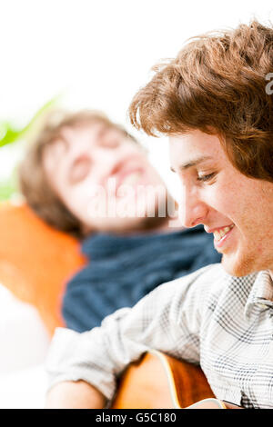 Beau jeune homme qui joue de la guitare pour un ami ou un frère comme ils se détendre ensemble à la maison, Close up profil face Banque D'Images