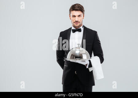 Young waiter in tuxedo holding plateau avec cloche métallique et une serviette Banque D'Images