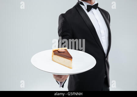 Waiter in tuxedo avec bowtie maintenant la plaque avec du gâteau Banque D'Images