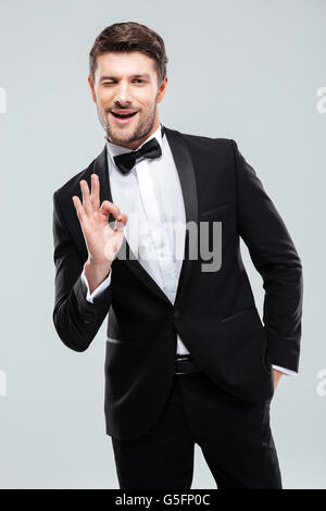 Smiling young man in tuxedo avec bowtie clins et montrant ok sign Banque D'Images