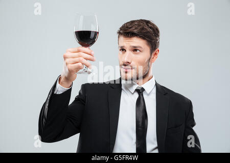 Jeune homme sérieux sommelier dégustation suite vin rouge dans le verre sur fond blanc Banque D'Images