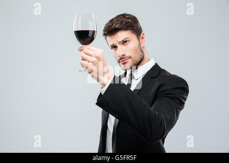 Jeune homme concentré et dégustation sommelier vin rouge en regardant le verre sur fond blanc Banque D'Images