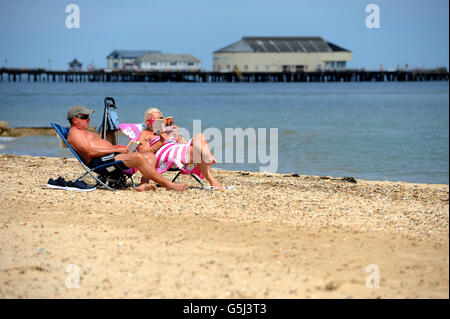 Un couple de soleil sur la plage car ils profiter du beau temps à Clacton-on-Sea dans l'Essex. Banque D'Images