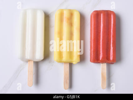 Vue du haut de trois différents ice pop sur un comptoir en marbre. Rouge, jaune et blanc pop à saveur de fruits. Banque D'Images