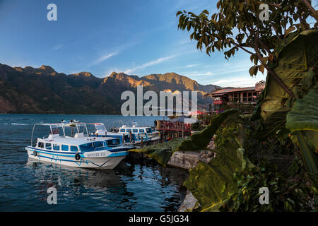 Coucher du soleil peint les falaises du cratère qui forme le lac Atitlan dans le sud de l'guatemala. Un taxi d'eau est fixé à san pedro la la Banque D'Images