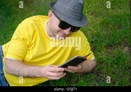 Jeune homme intelligent dans un T-shirt jaune avec le téléphone sur l'herbe Banque D'Images