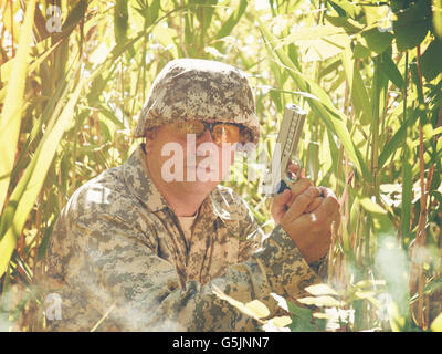 Un soldat de l'homme tient une arme à la main dans la forêt avec de hautes herbes à l'extérieur pour la défense, la sécurité ou la lutte contre le concept de guerre. Banque D'Images