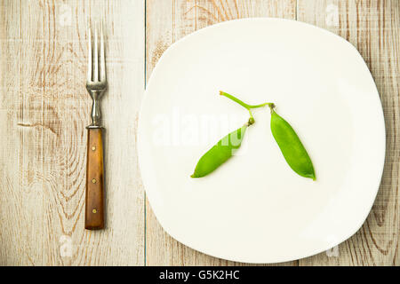 Les gousses de pois verts et la fourche sur la plaque blanche. Banque D'Images