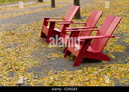 Chaises adirondack rouge situé parmi des piles de feuilles d'automne Banque D'Images
