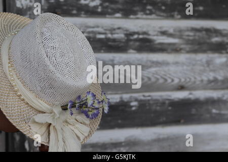 Womans antique white hat avec des fleurs contre gris patiné bois d'évitement grange Banque D'Images