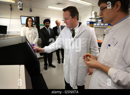 Le Premier ministre David Cameron (deuxième à droite) se tient aux côtés du Dr James Hadfield (à droite), qui utilise une machine personnelle de séquençage du génome lors d’une visite au cancer Research UK Cambridge Research Institute, à Cambridge, en Angleterre. Banque D'Images