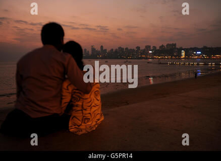 Un couple regarde le coucher de soleil derrière les collines de Malaba (le Manhatton de Mumbai) depuis le mur costal sur Marine Drive à Mumbai, Inde Banque D'Images