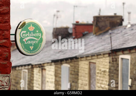 Un panneau de bière provenant d'un magasin surplombe des maisons à arraisonner dans une rue d'Accrington dans le Lancashire. Banque D'Images