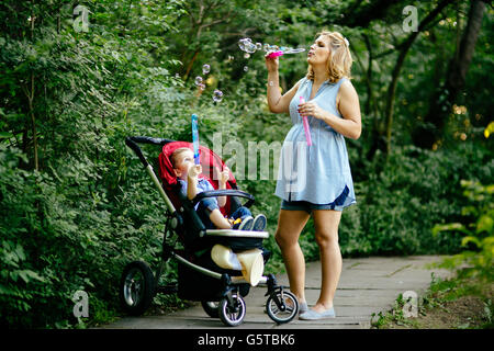 Happy pregnant woman soufflant des bulles de savon avec les enfants dans la nature Banque D'Images