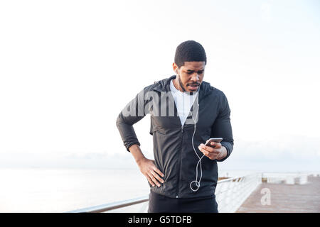 Les jeunes africains concentrés sportsman à écouter de la musique de téléphone recevez le standing on pier Banque D'Images