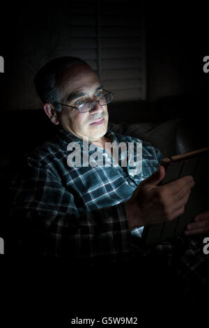 Middle aged man wearing pajamas Tablette de lecture la nuit au lit avec expression grave Banque D'Images