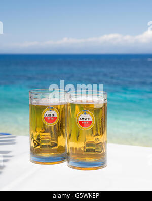 Pinte de bière Amstel glasses on white table au bar de plage avec mer en arrière-plan Banque D'Images