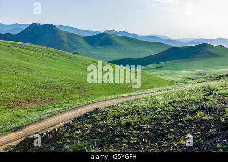 La route sinueuse à travers les collines luxuriantes de steppe de Mongolie centrale Banque D'Images