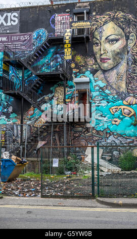 Un mur d'un bâtiment qui a été couvert dans l'art de mur avec des signes d'un salon de tatouage sur l'escalier de secours. Banque D'Images