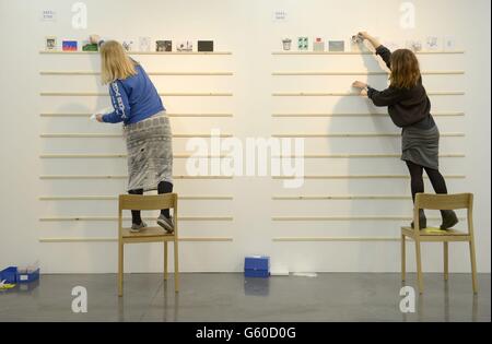 Des assistants d'exposition accrochent des œuvres d'art à l'exposition RCA Secret 2013 de la maison Dyson du collège, bâtiment du sud de Londres.2,700 cartes postales seront vendues de manière anonyme dans le cadre de l'événement pour &Pound;45 chacune et parmi elles seront des œuvres de David Bailey, Nick Park, Paul Smith, John Squire et Manolo Blahnik. Banque D'Images