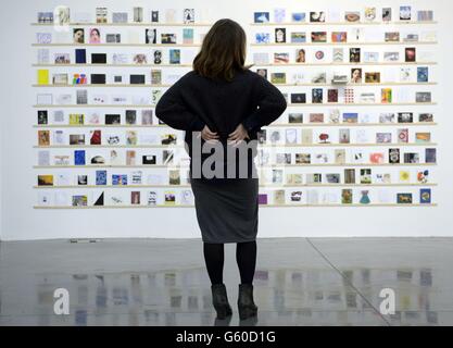 Un assistant d'exposition admire des œuvres d'art à l'exposition RCA Secret 2013 à la Dyson House du collège, bâtiment du sud de Londres.2,700 cartes postales seront vendues de manière anonyme dans le cadre de l'événement pour &Pound;45 chacune et parmi elles seront des œuvres de David Bailey, Nick Park, Paul Smith, John Squire et Manolo Blahnik. Banque D'Images