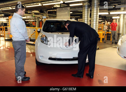 Le Premier ministre David Cameron attache un insigne Nissan à l'avant d'une voiture électrique Nissan Leaf lors d'une visite à l'usine Nissan de Sunderland. Banque D'Images