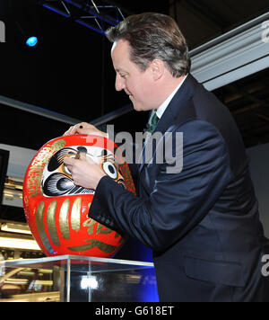 Le Premier ministre David Cameron se colore dans l'œil d'une poupée Daruma, qui fait partie d'une tradition japonaise heureuse pour marquer la fin d'un projet lors d'une visite à l'usine Nissan, Sunderland. Banque D'Images