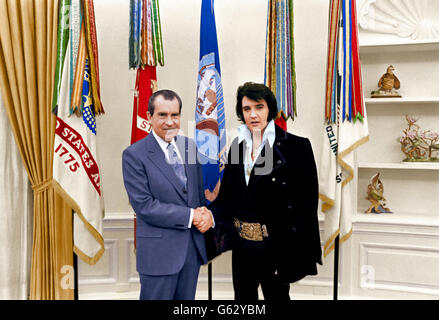 Elvis Presley, serre la main du président américain Richard M. Nixon en tant que membre du personnel de la Maison Blanche Egil Krogh regarde sur dans le bureau ovale à la Maison Blanche le 21 décembre 1970 à Washington, DC. (Note au rédacteur : l'image original est en noir & blanc et a été colorisée artificiellement pour simuler une authentique image couleur. Rien d'autre n'a été changé ou modifié.) Banque D'Images