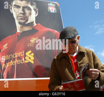 Un fan de Liverpool lit le programme de la journée de match à côté d'une grande affiche du capitaine du club Steven Gerrard Banque D'Images