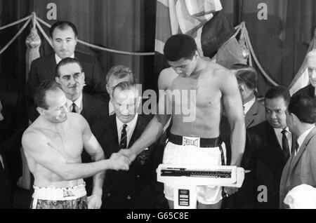 Le champion américain du monde à fort poids, Muhammad Ali (14 pierres 5&#189; livres) sur la balance et le challenger Henry Cooper (13 pierres 6 livres) se met à serrer la main au Weight-in de l'Odeon à Leicester Square, Londres, pour leur combat du titre mondial au stade Highbury d'Arsenal. Banque D'Images