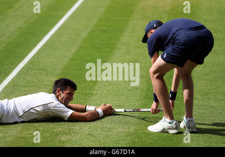 Le Novak Djokovic de Serbie est aidé hors du sol par un garçon de balle après s'être étiré pour un tir dans son match contre Juan Martin Del Potro d'Argentine pendant le onze jour des championnats de Wimbledon au All England Lawn tennis and Croquet Club, Wimbledon. Banque D'Images