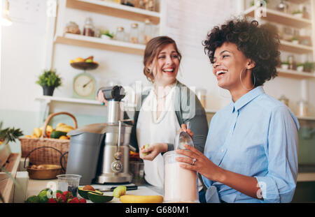 Deux jeunes femmes parlant et souriant tout en travaillant au comptoir du bar. Ils sont en train de préparer des jus de fruits. Banque D'Images