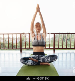 Young woman sitting on floor in yoga pose les mains jointes au-dessus. Modèle féminin de remise en forme faire du yoga. Banque D'Images