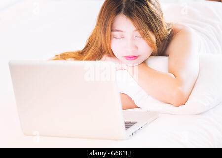 Belle jeune femme en peignoir sont endormis pendant l'utilisation d'ordinateur portable dans le lit à la maison Banque D'Images