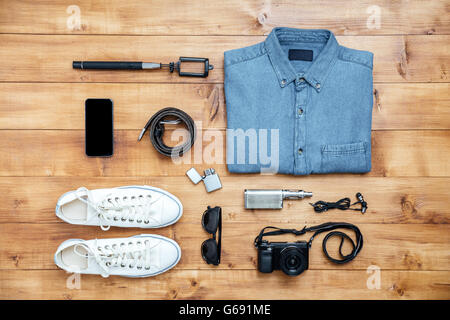 Concept de voyage chaussures, T-shirt, téléphone portable, lunettes, ceinture, briquet, appareil photo, écouteurs, narguilé, stick selfies sur le bureau Banque D'Images