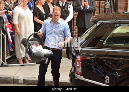 Le duc de Cambridge porte son nouveau fils, le prince George de Cambridge, à la voiture, tandis que lui et la duchesse de Cambridge quittent l'aile Lindo de l'hôpital St Mary à Londres. Banque D'Images