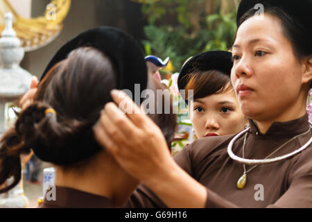 Femme en ao Dai prépare les filles pour la cérémonie religieuse au centre du Vietnam Banque D'Images