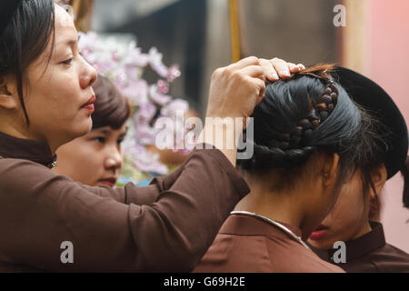 Femme en ao Dai prépare les filles pour la cérémonie religieuse au centre du Vietnam Banque D'Images